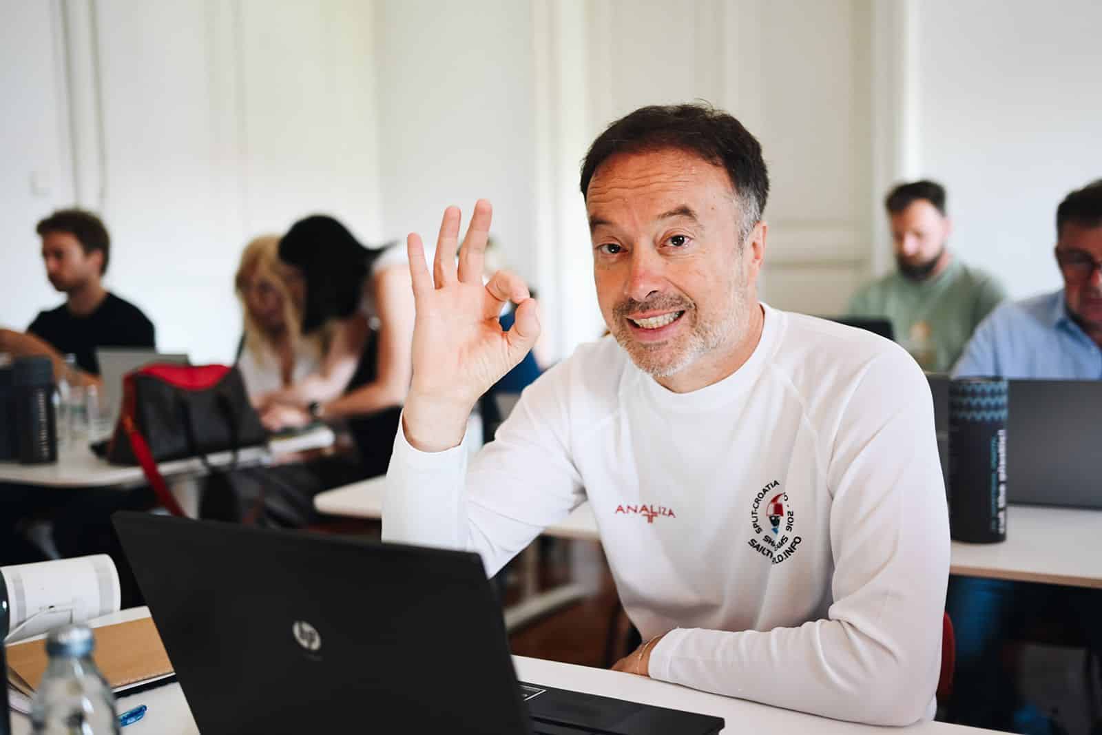 A participant gives an OK sign to the camera, an open laptop in front of them